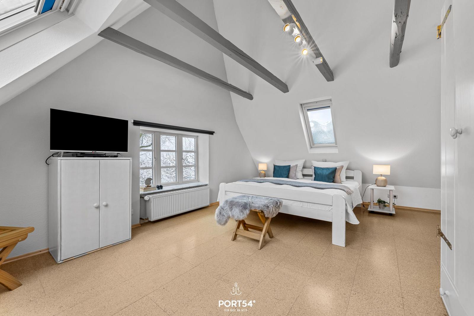 Schlafzimmer mit Dachschrägen, Bett, Fernseher und Fenster.