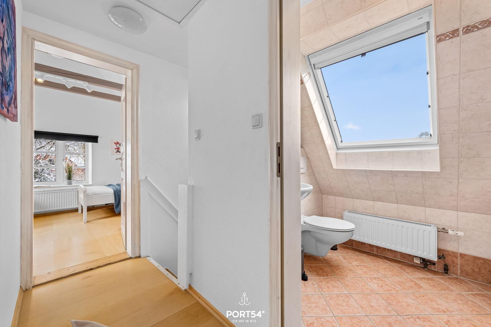 Badezimmer mit Dachfenster und Toilette. Nebenraum mit Bett und Fenster.