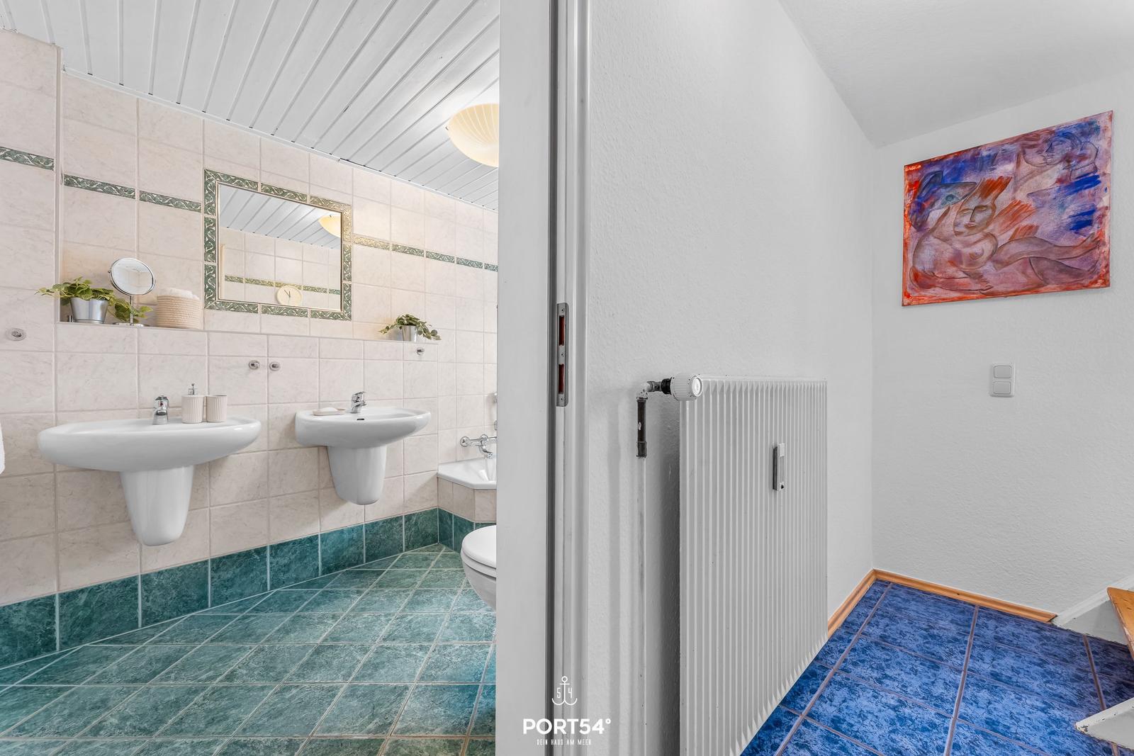 Badezimmer mit zwei Waschbecken und Toilette. Fliesenboden und Wandbild.
