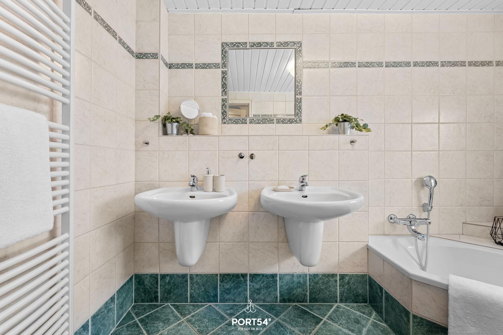 Badezimmer mit zwei Waschbecken, Badewanne und Heizkörper.