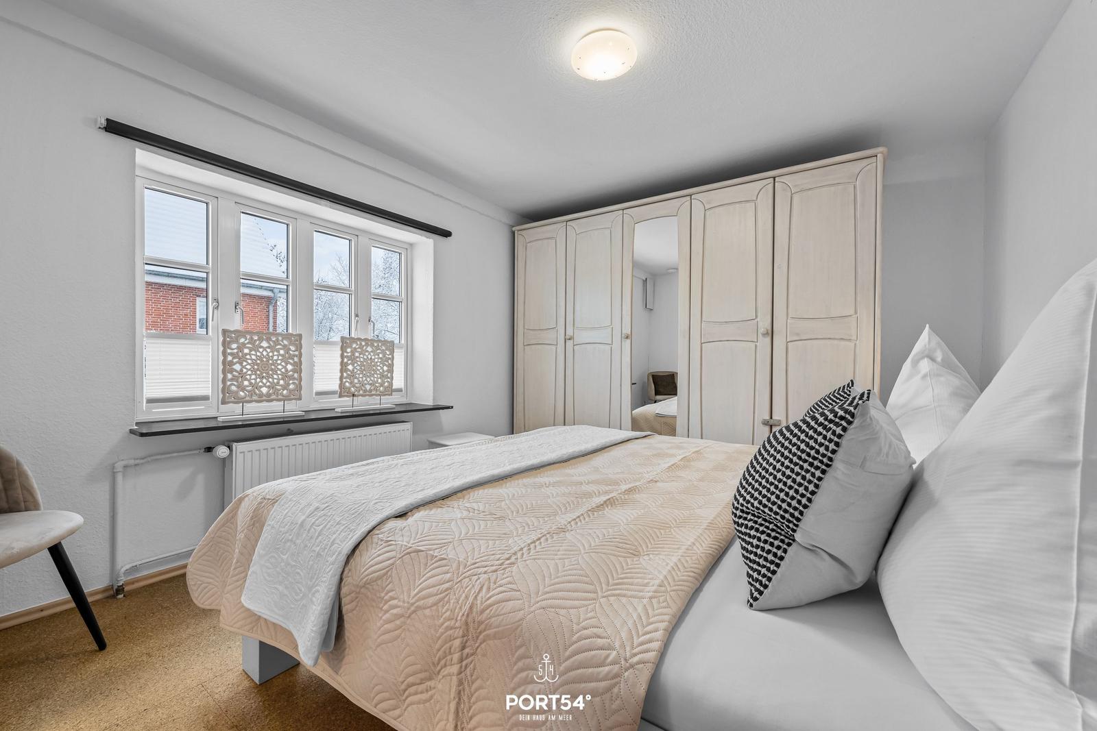 Schlafzimmer mit Bett, Kleiderschrank und Fenster.