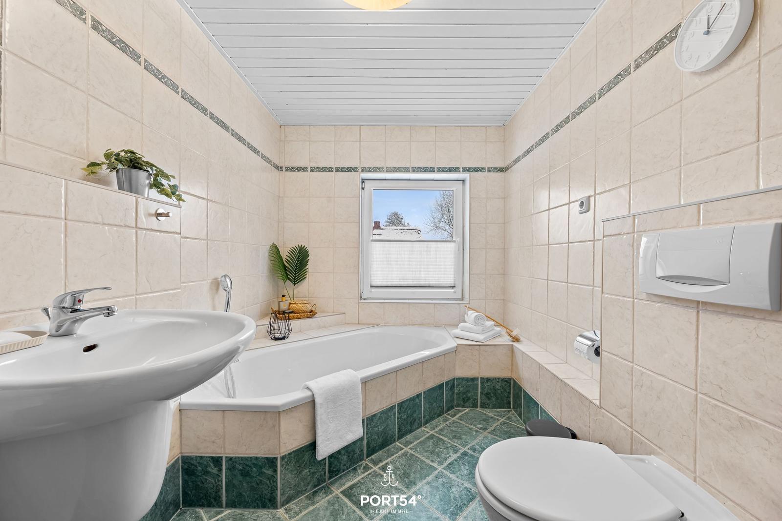 Badezimmer mit Badewanne, Waschbecken und Toilette. Fenster mit Blick nach draußen.