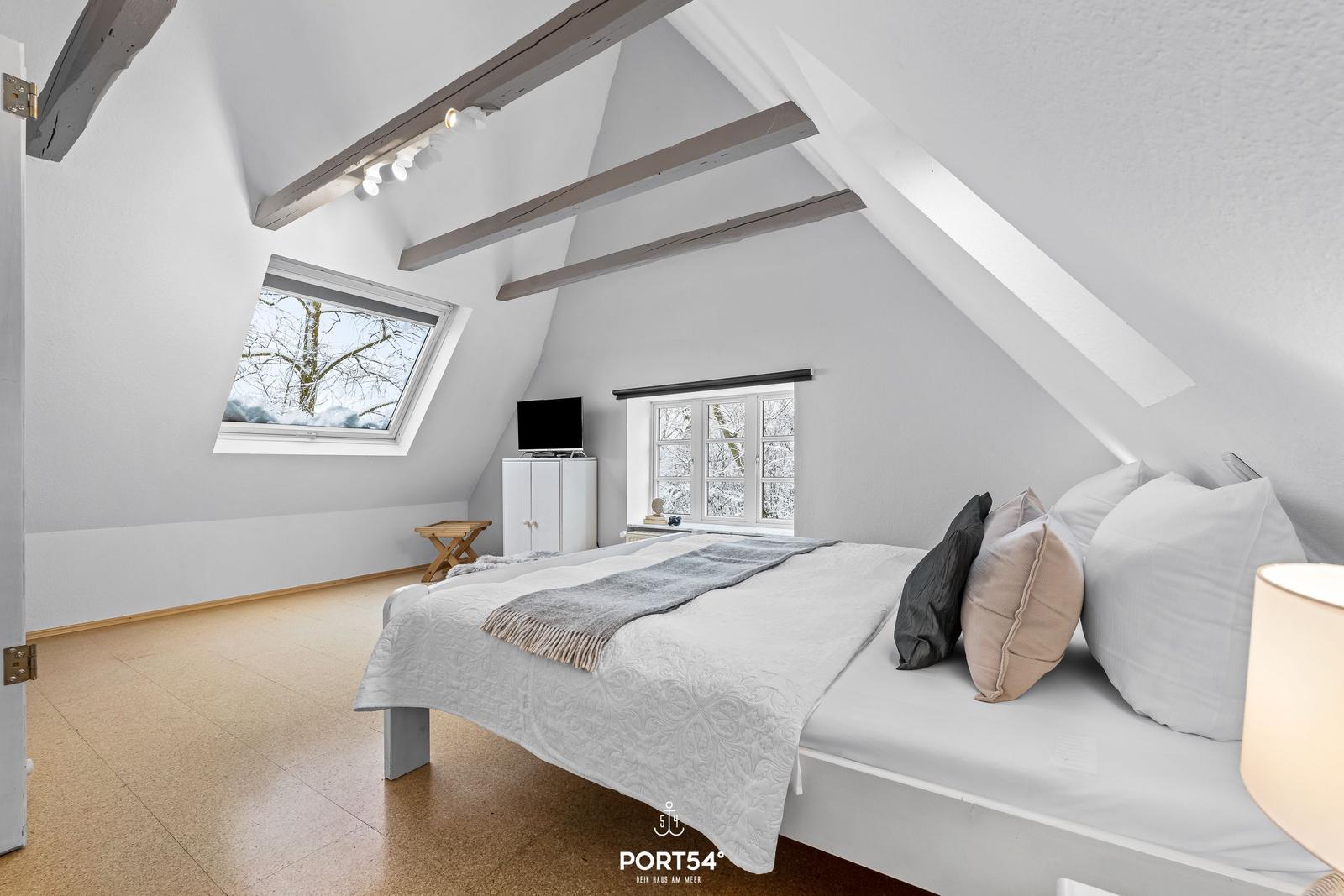 Schlafzimmer mit Dachschrägen, Fenster und Bett.