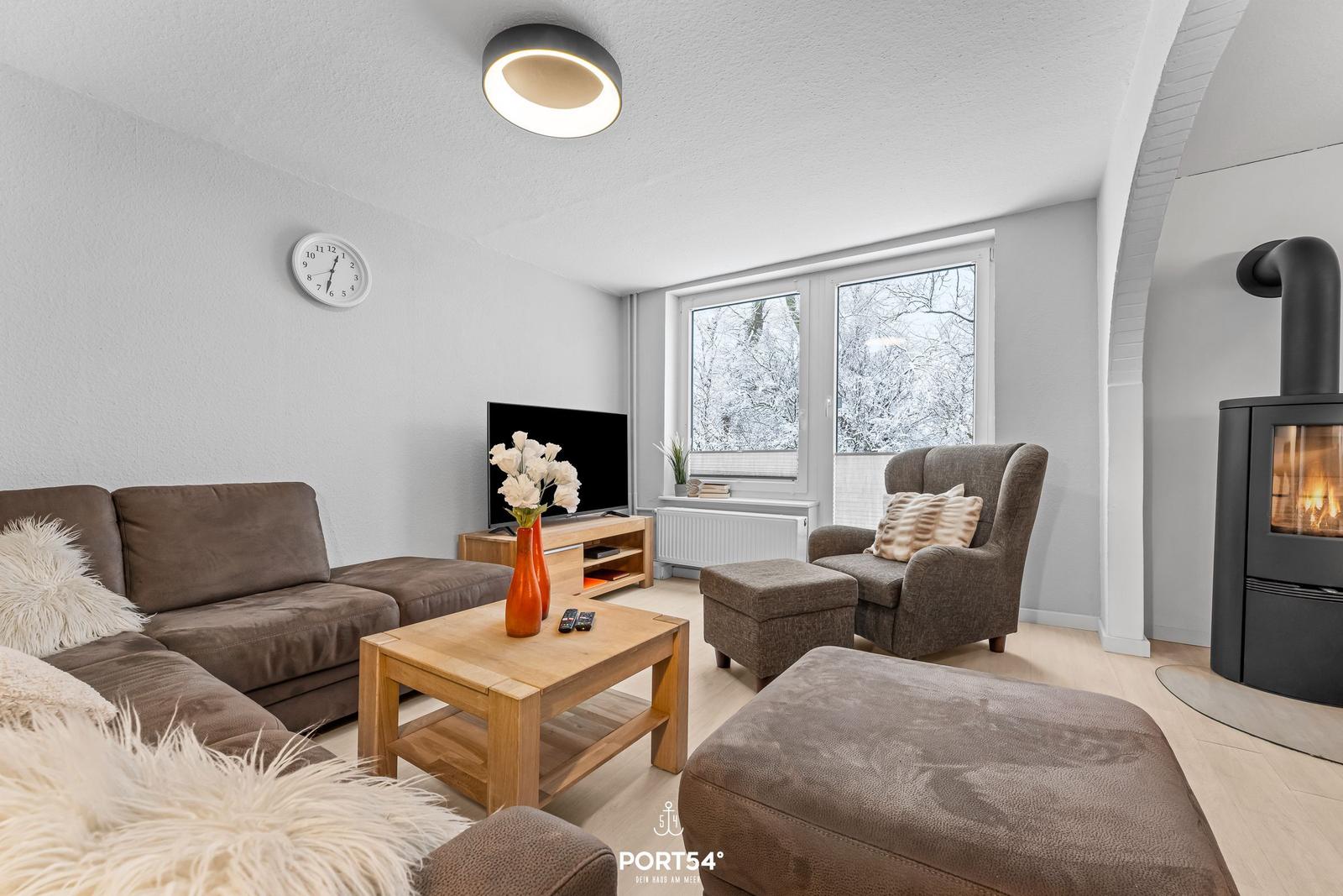 Wohnzimmer mit Sofa, Sessel und Kaminofen. Fenster mit Blick auf Schnee.