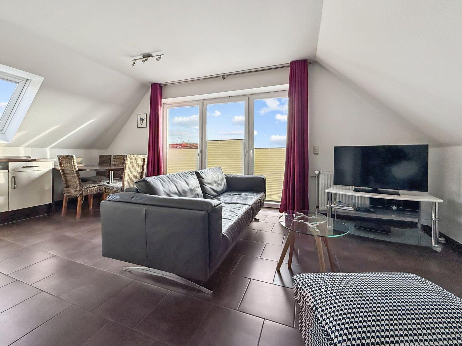 Wohnung mit Sofa, Fernseher und Essbereich unter Dachschrägen.