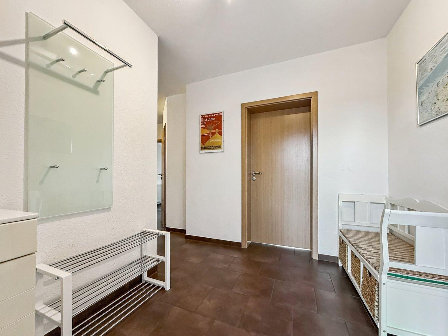 Flur mit Garderobe, Bänkchen und Tür. Wandbild und Bodenfliesen sichtbar.