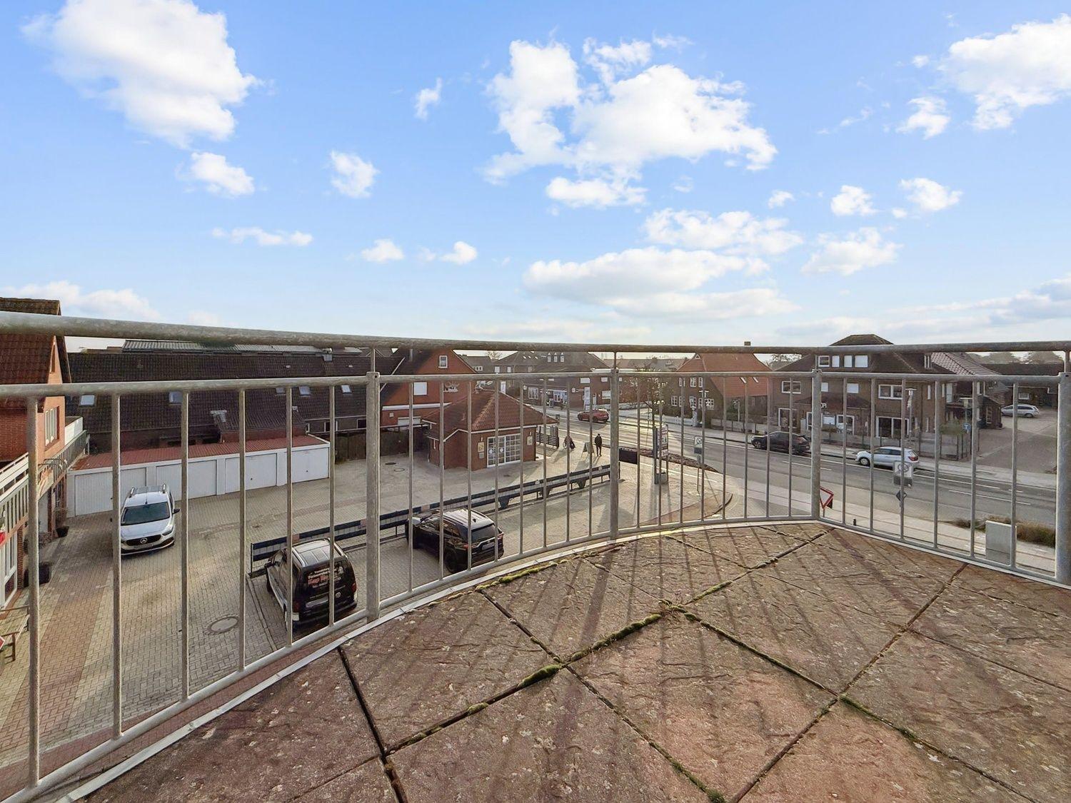 Terrasse mit Blick auf Straße und umliegende Gebäude unter blauem Himmel mit weißen Wolken.