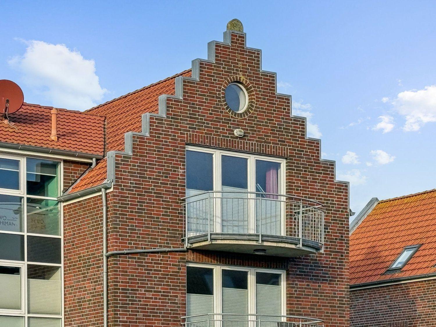 Rotes Ziegeldach und Backsteinfassade mit Balkon und runden Fenster.