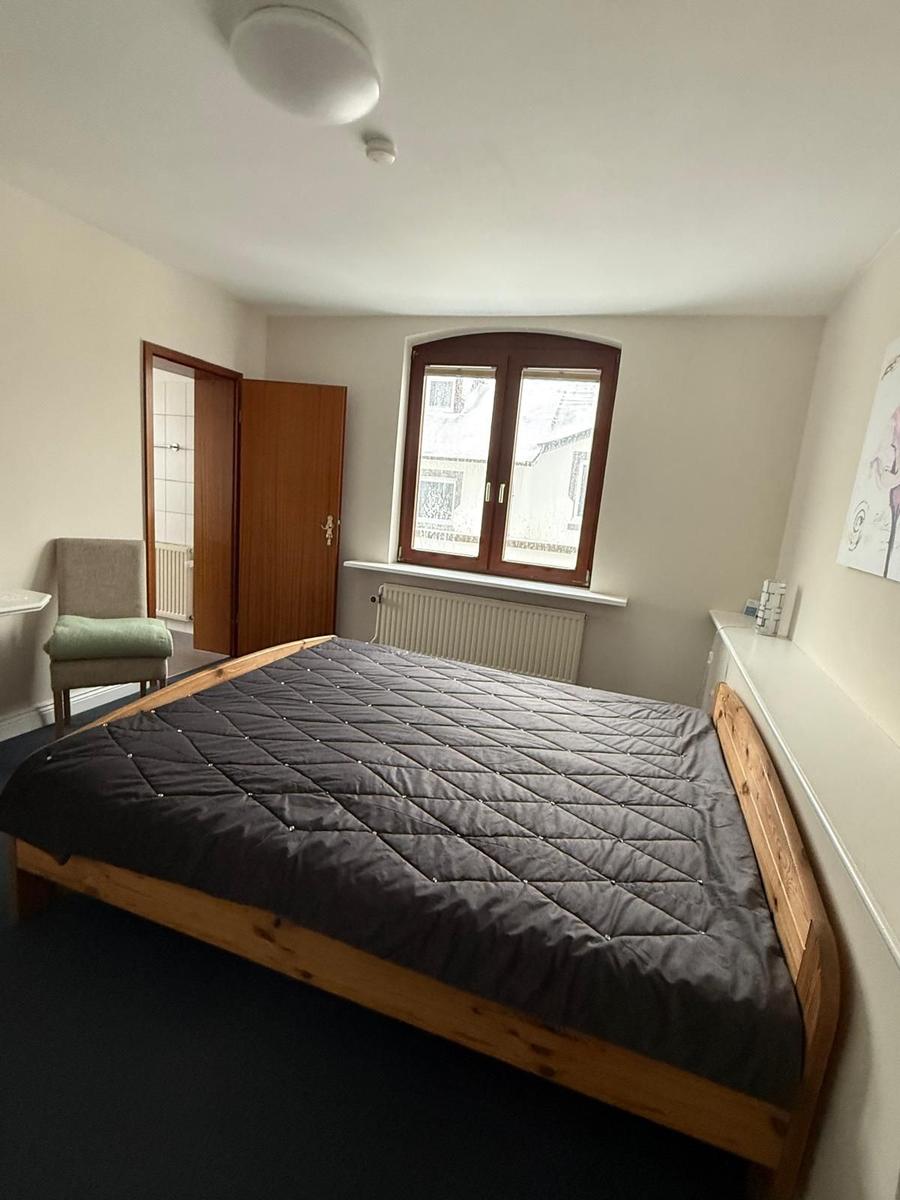 Schlafzimmer mit Holzbett, Fenster und Stuhl.