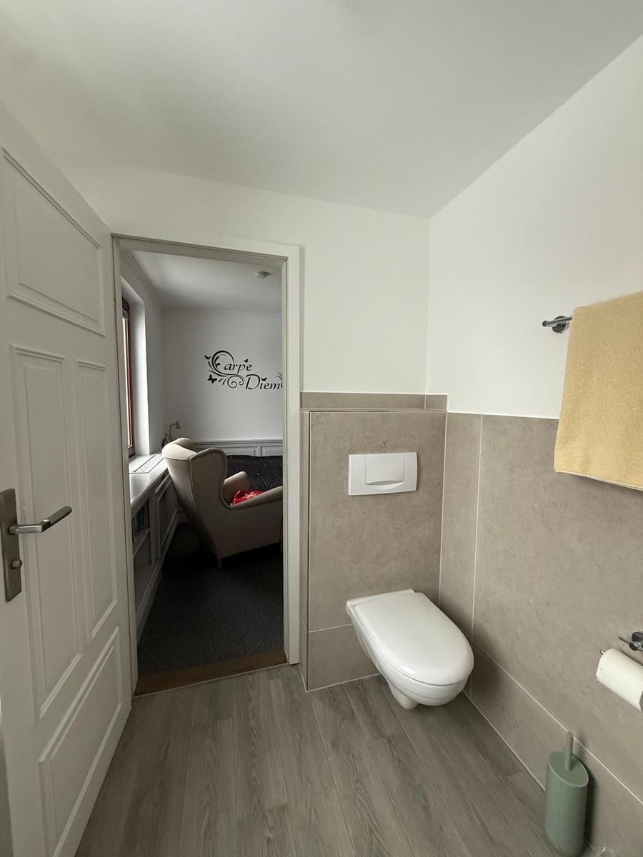 Badezimmer mit Toilette und Blick in Schlafzimmer mit Sessel.