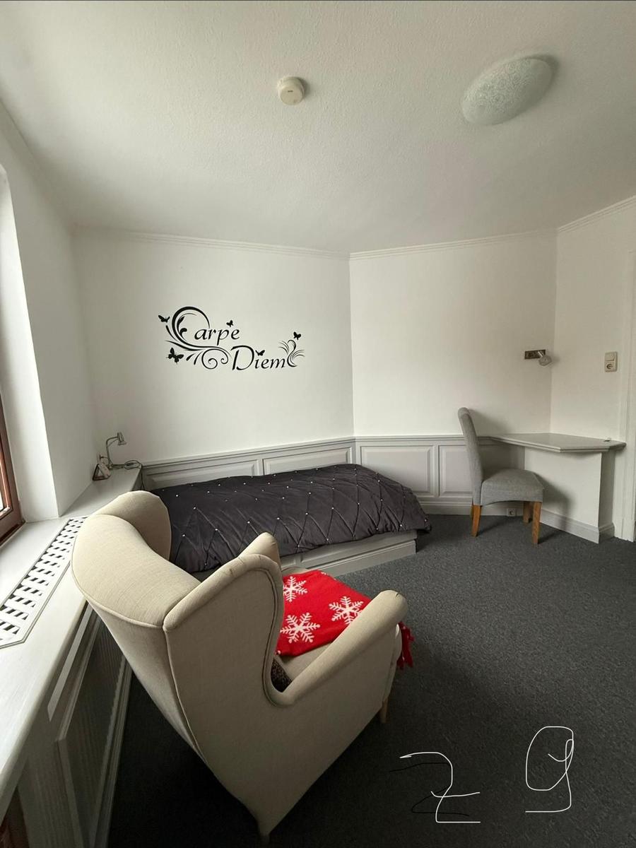 Zimmer mit Bett, Sessel, Schreibtisch und Wanddekoration.