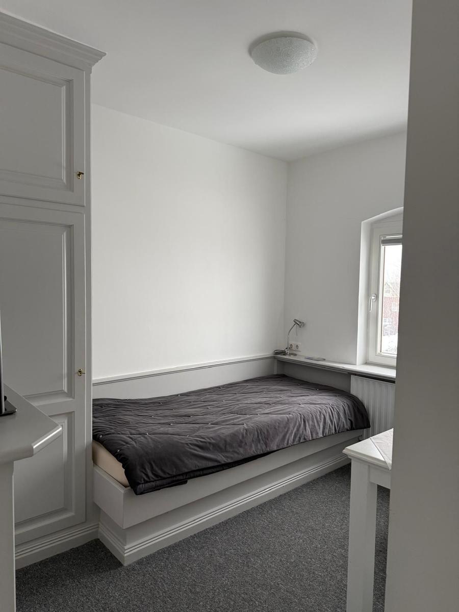 Schlafzimmer mit Bett, Schrank und Fenster. Bodenbelag und Wände sind weiß.