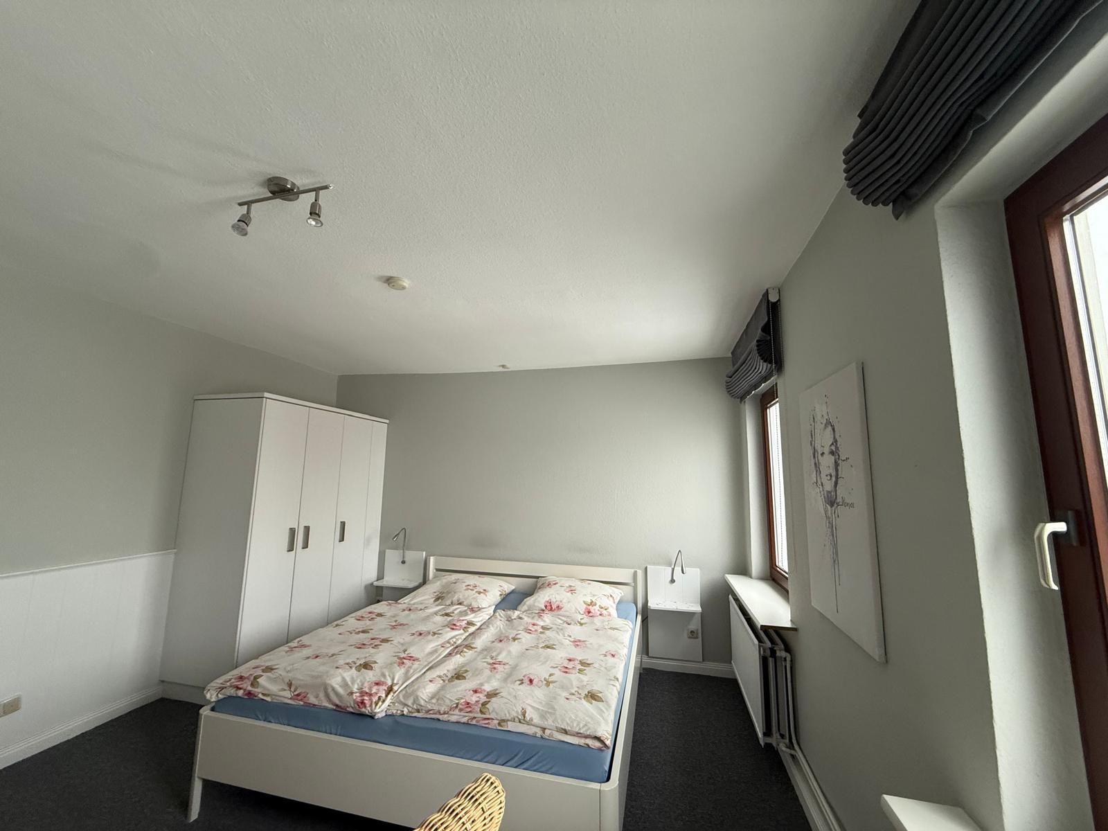 Schlafzimmer mit Doppelbett, Kleiderschrank und Fenster.