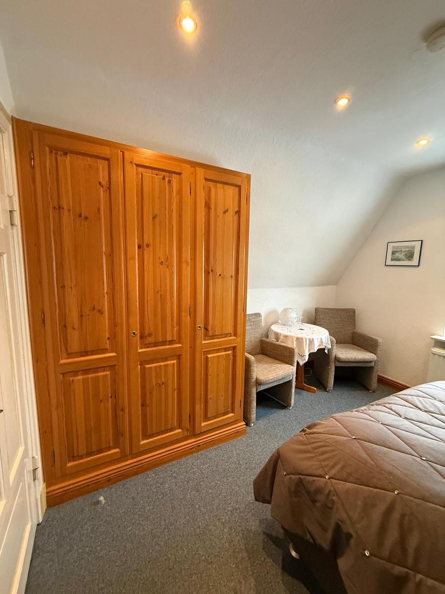 Schlafzimmer mit Holzschrank, Tisch und zwei Stühlen unter Dachschrägen.