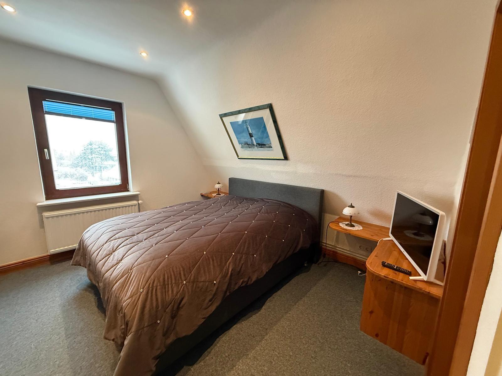 Schlafzimmer mit Bett, Fenster und Fernseher auf Holzschrank