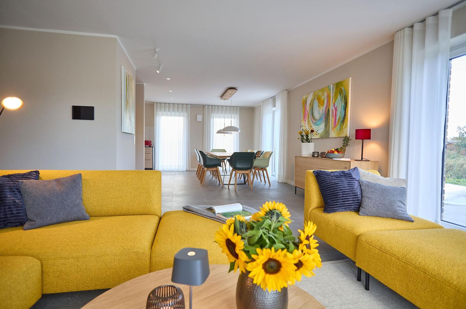 Wohn- und Essbereich mit gelben Sofas, Sonnenblumen und moderner Einrichtung.