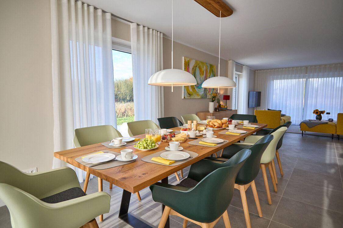 Esszimmer mit langem Tisch, Stühlen und Blick auf Garten.