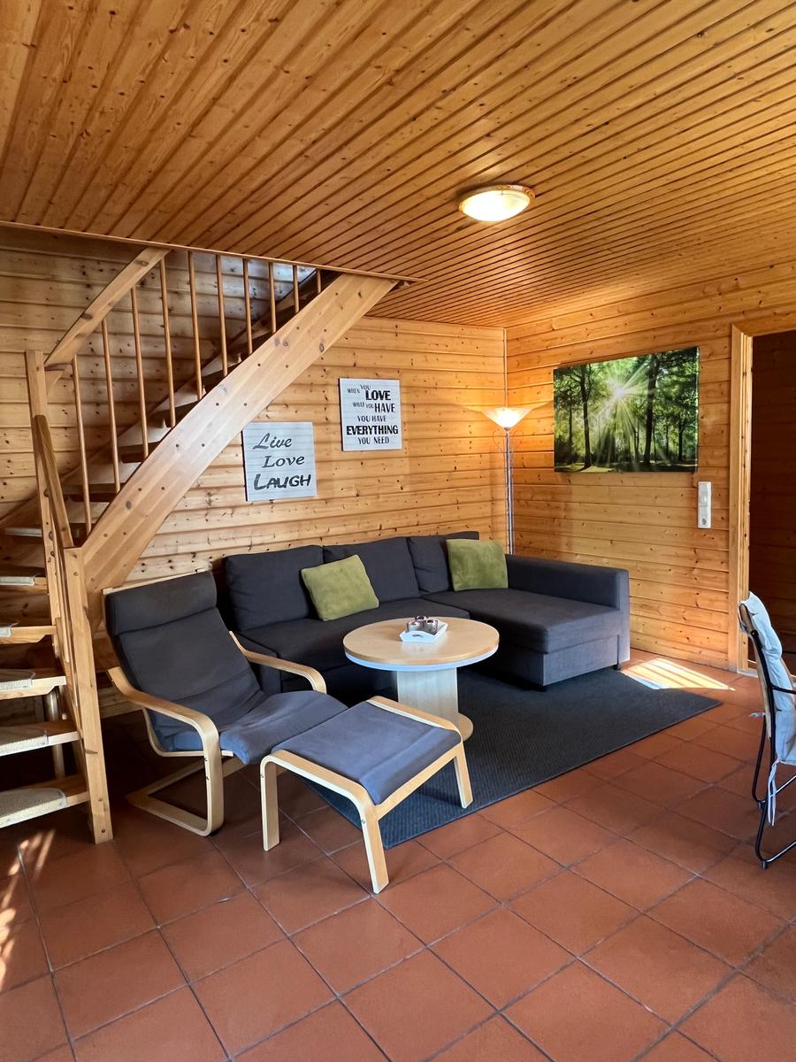 Wohnzimmer mit Sofa, Sessel und Treppe zu einer oberen Etage.