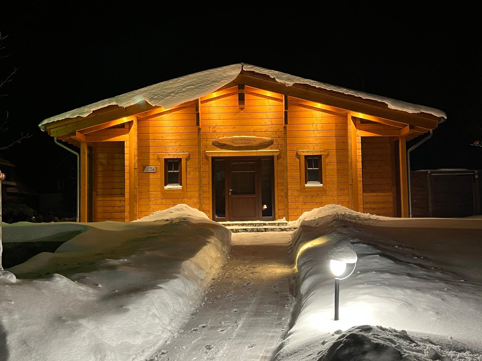 Holzhütte mit Schnee, beleuchteter Eingang und Weg