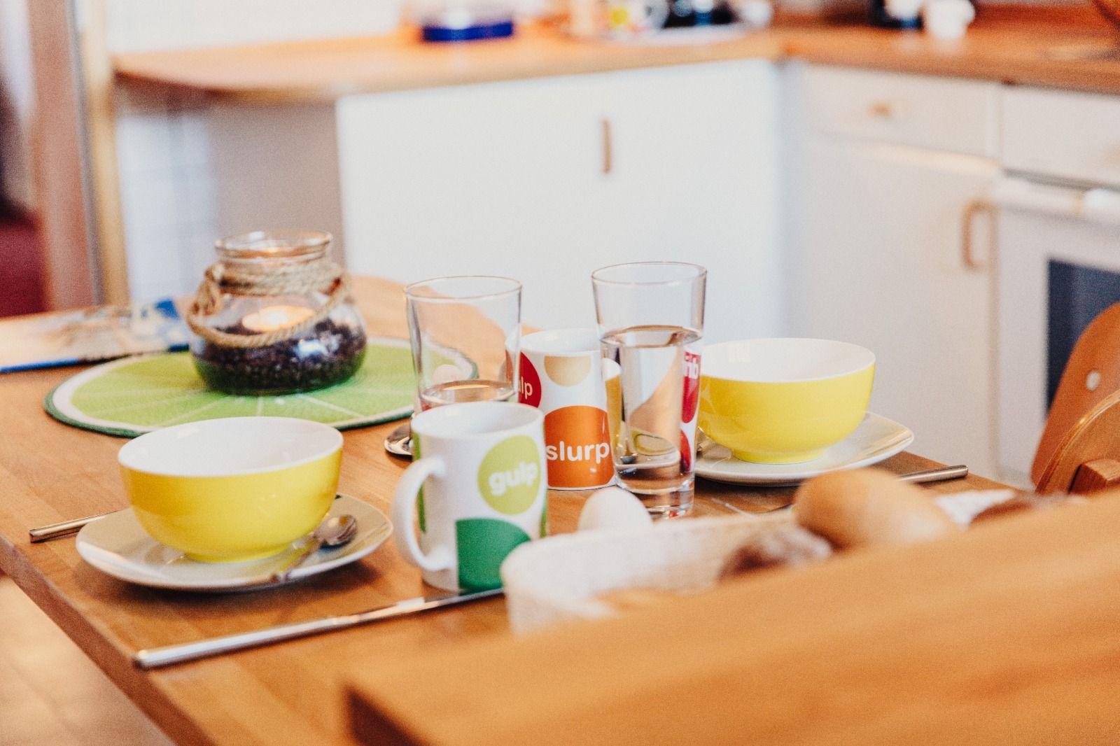 Esstisch mit Tassen, Tellern und einem Kerzenhalter.