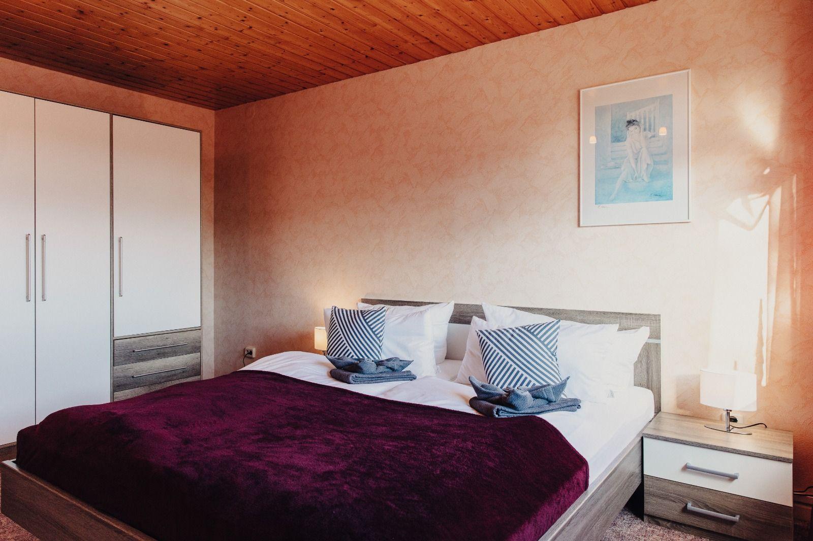 Schlafzimmer mit Bett, Nachttisch und Kleiderschrank. Holzdecke und Wandbild.