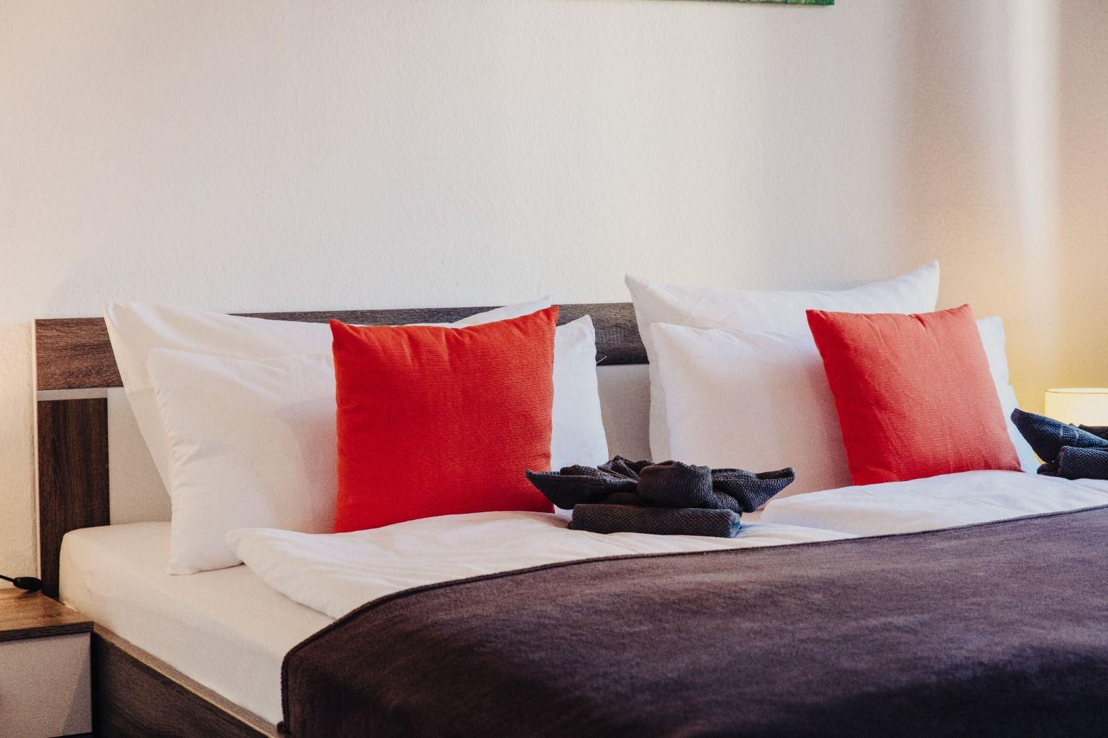 Doppelbett mit weißen Kissen und zwei roten Kissen.
