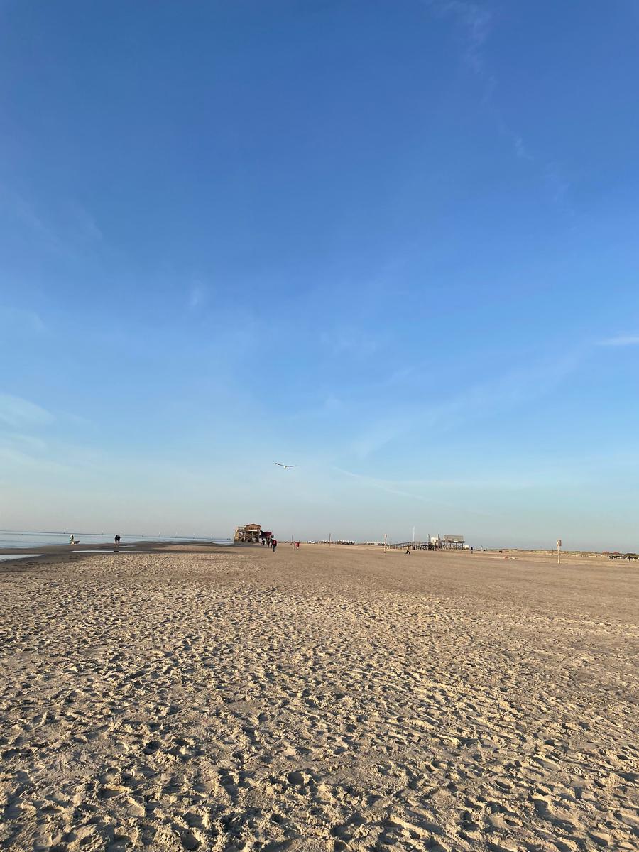Weiterer Blick auf den Strand mit klarem Himmel und einigen Personen in der Ferne.