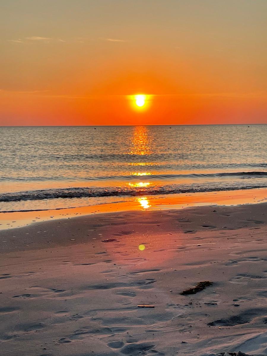 Sonnenuntergang über dem Meer mit Reflexion auf Sand und Wasser.