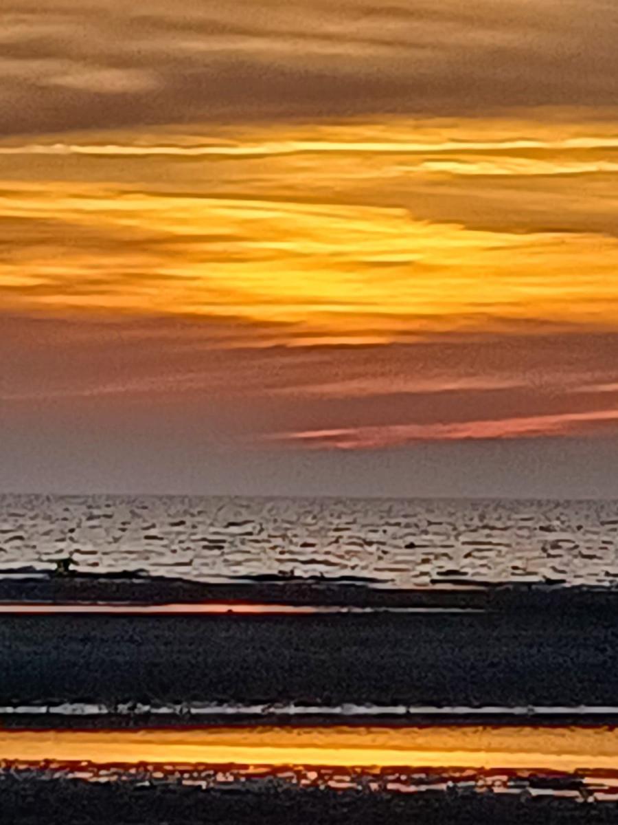 Sonnenuntergang über dem Meer mit goldenen Wolken und spiegelnder Wasseroberfläche.