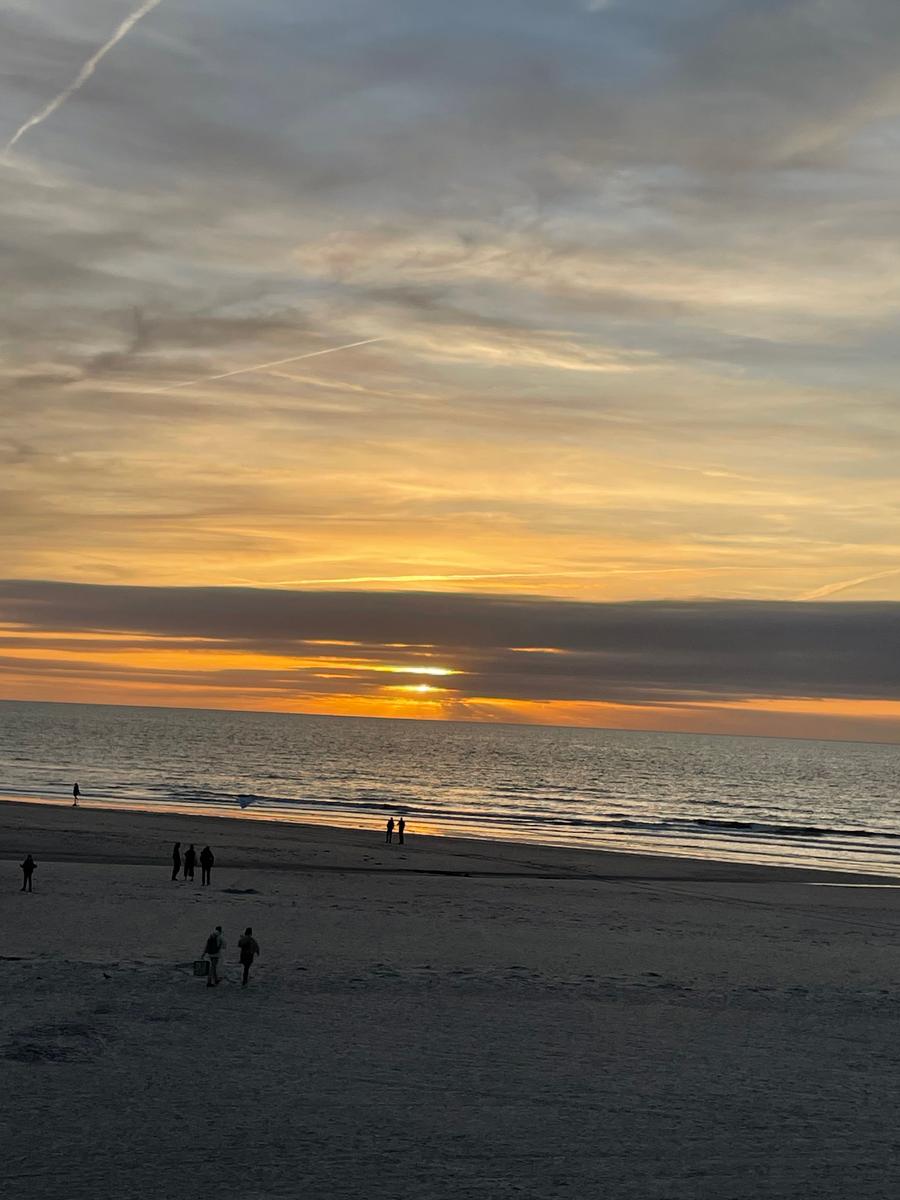 Sonnenuntergang am Strand mit wenigen Personen und dramatischem Himmel.
