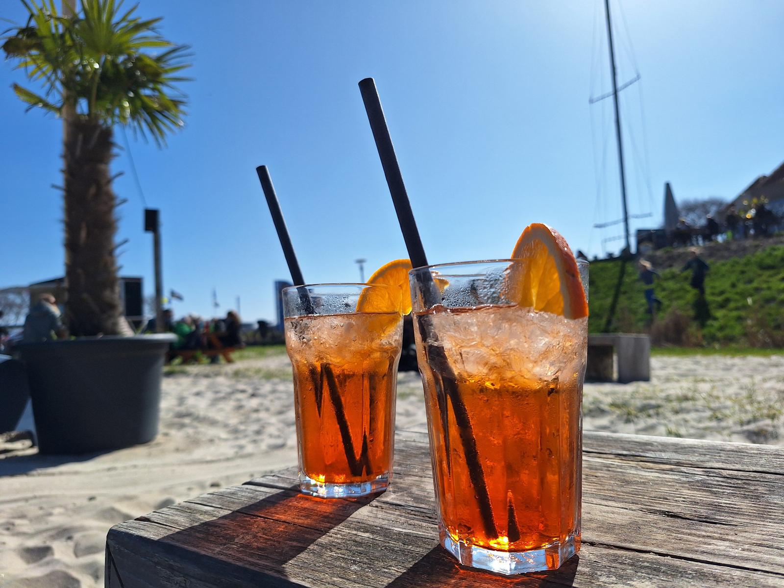 Zwei erfrischende Getränke mit Orangenscheiben stehen auf einem Holztisch am Strand.