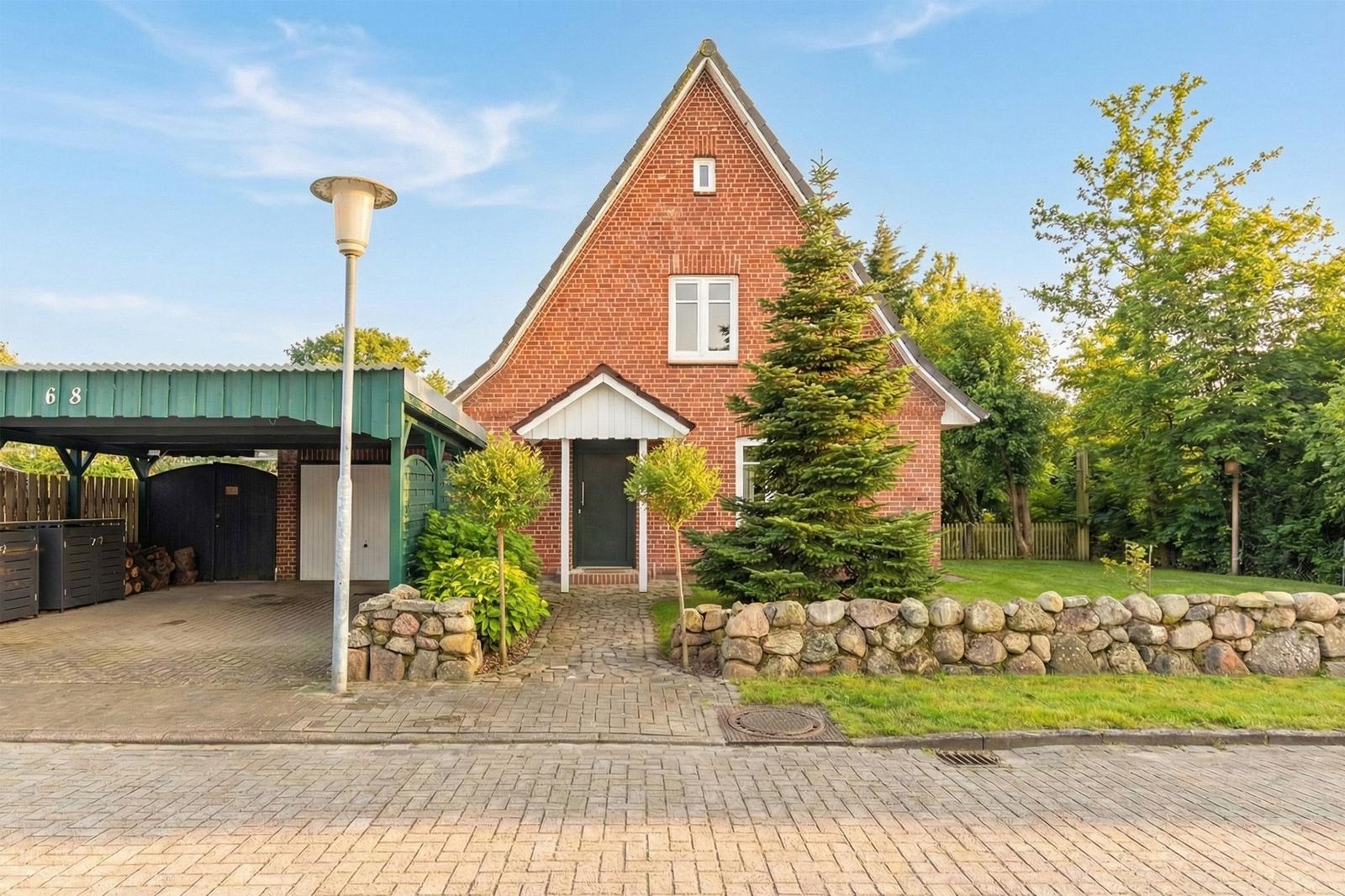Rotes Backsteinhaus mit Vorgarten, Steinmauer und Carport.