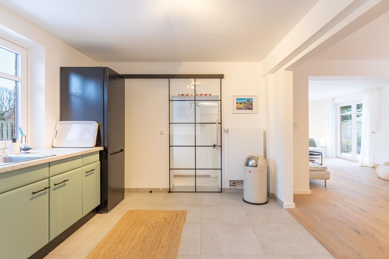 Küche mit grünen Schränken und schwarzer Kühlschranktür. Durchgang zur Wohnfläche mit Holzboden.