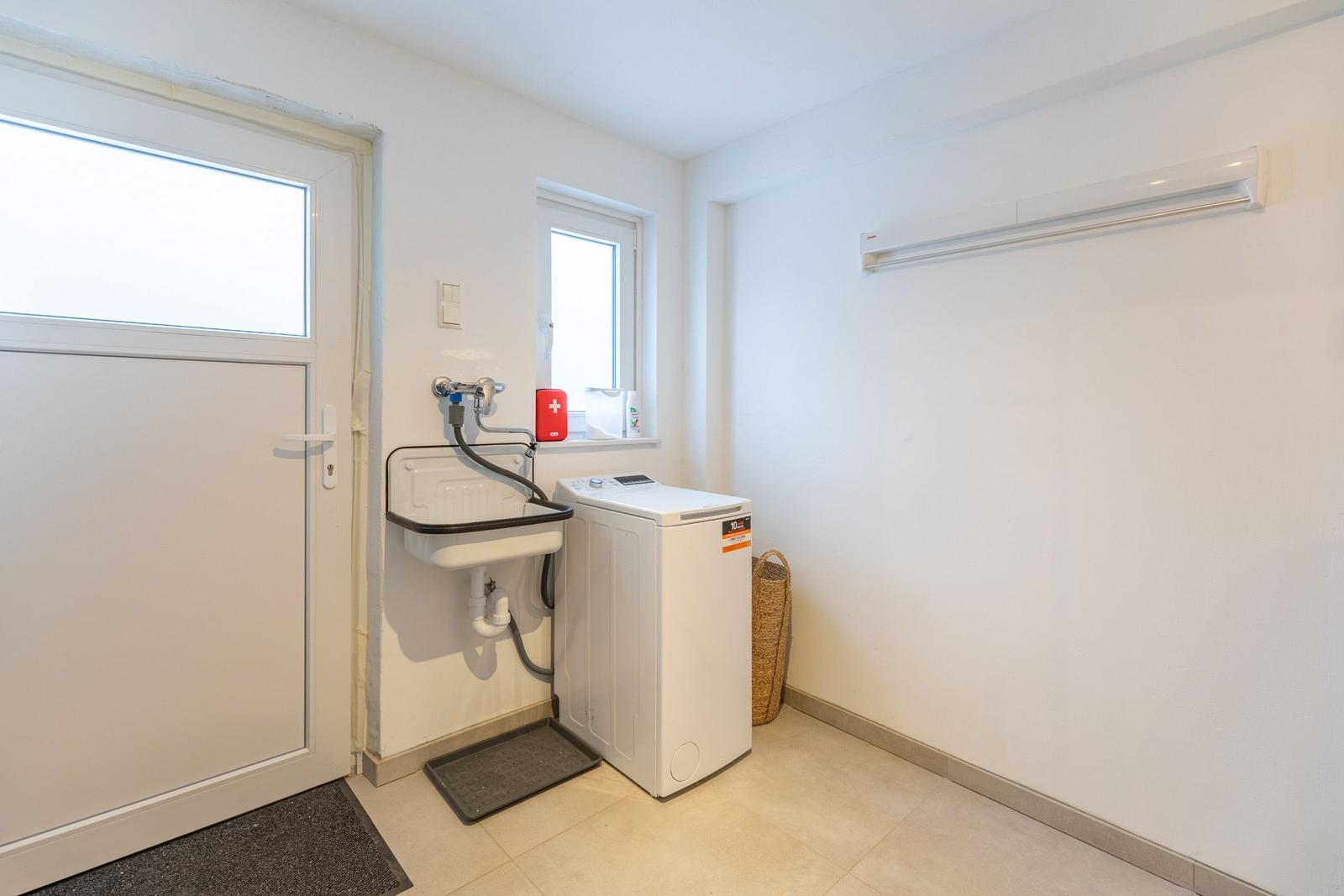 Waschraum mit Waschmaschine, Waschbecken und Fenster.