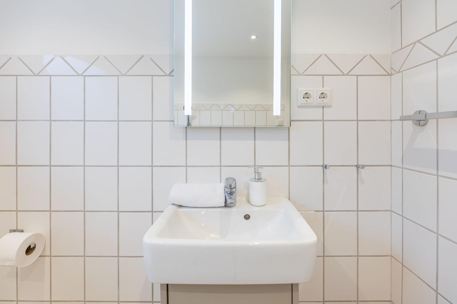 Badezimmer mit Waschbecken, Spiegel und Toilettenpapierhalter