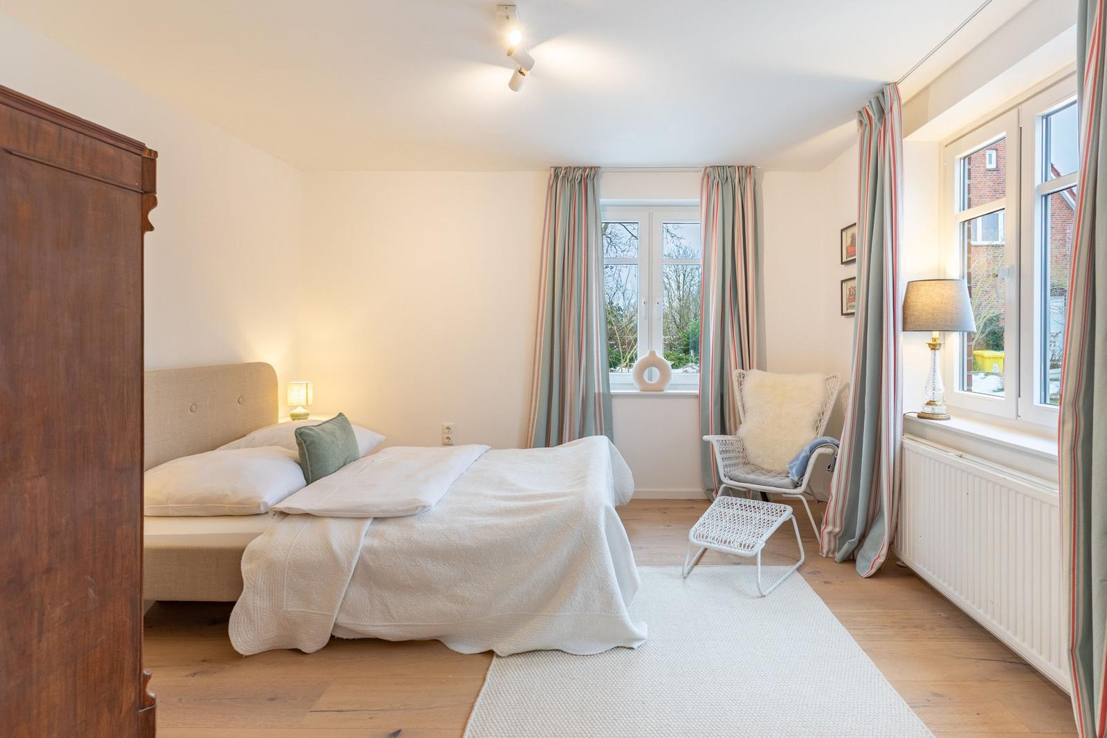 Schlafzimmer mit Bett, Stuhl und Fenstern.