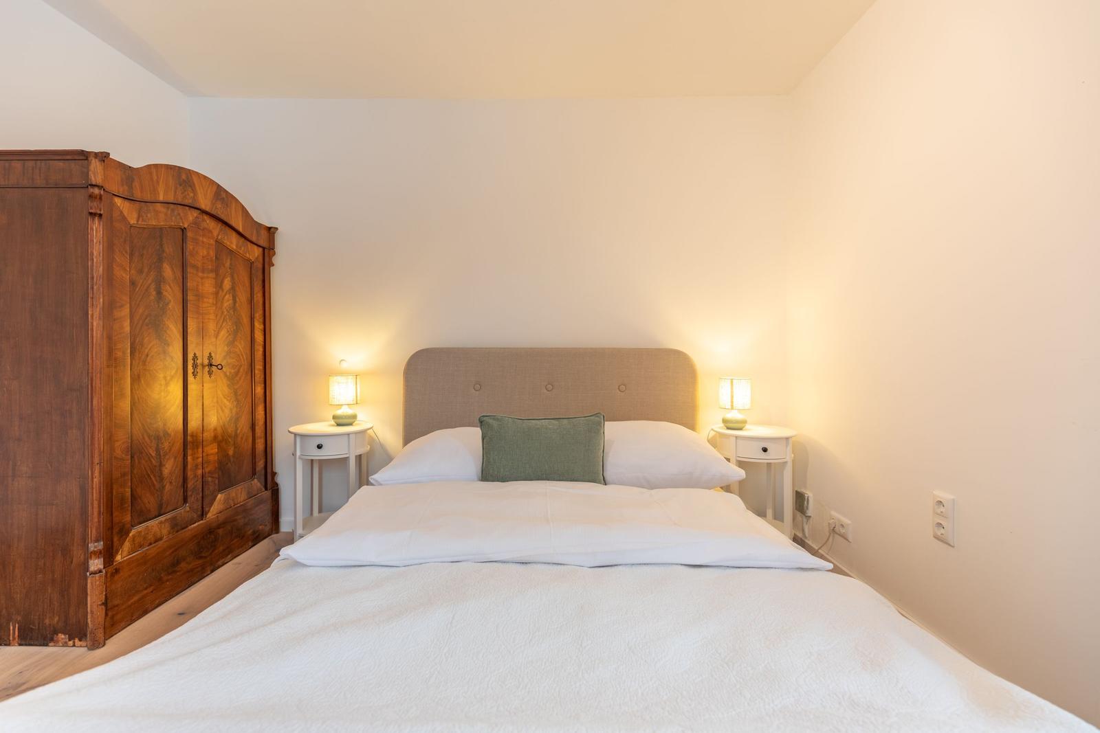 Schlafzimmer mit Bett, Nachttischen und antikem Schrank.