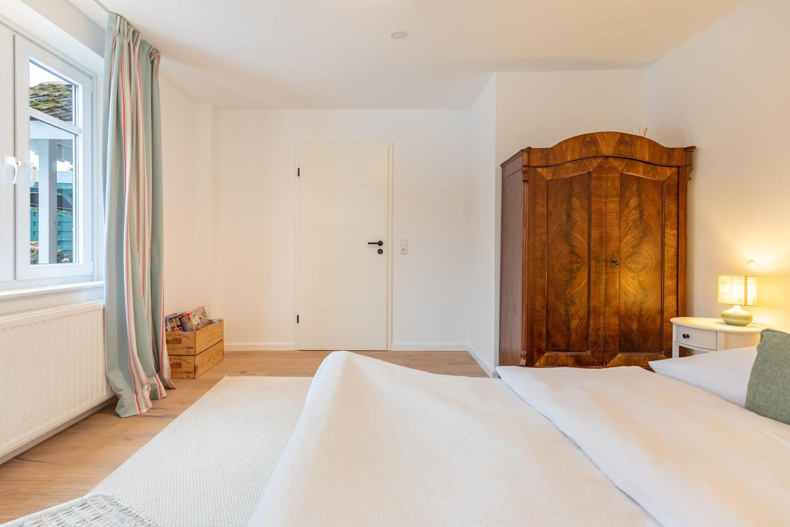 Schlafzimmer mit Bett, Holzschrank und Fenster mit Vorhängen.