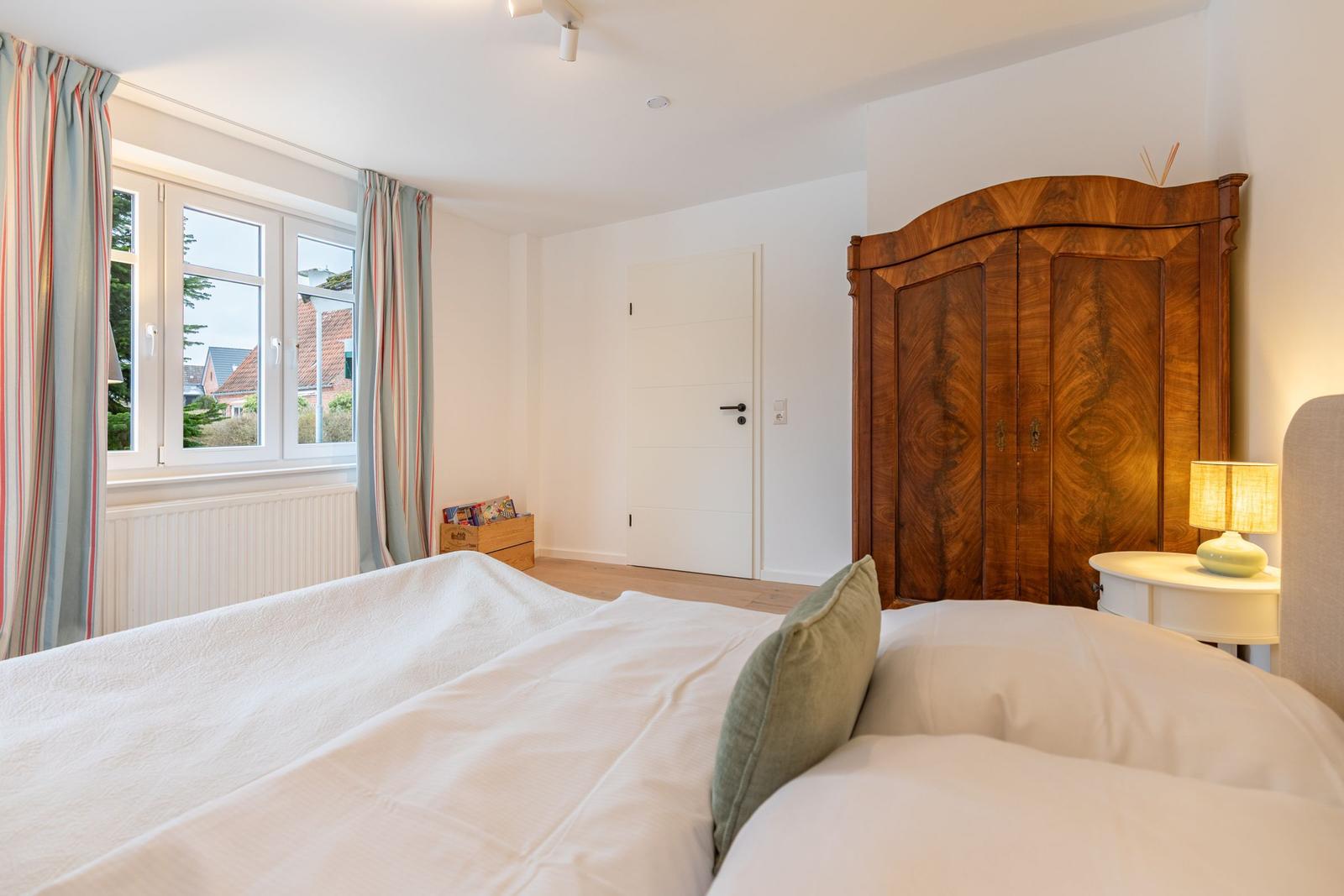 Schlafzimmer mit Bett, Holzschrank und Fenster mit Blick auf Außenbereich.