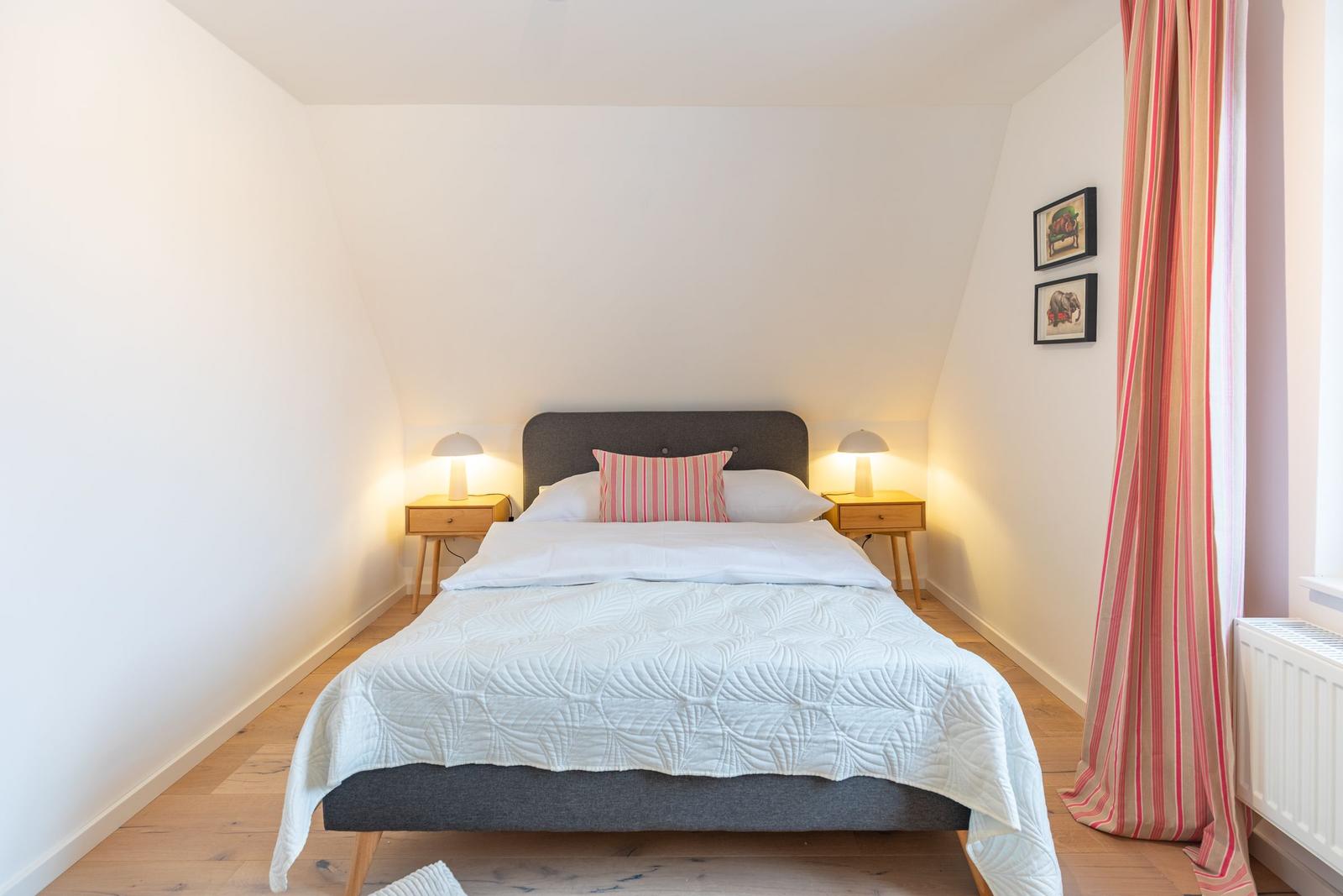 Schlafzimmer mit Bett, Nachttischen und Vorhängen an Fenster