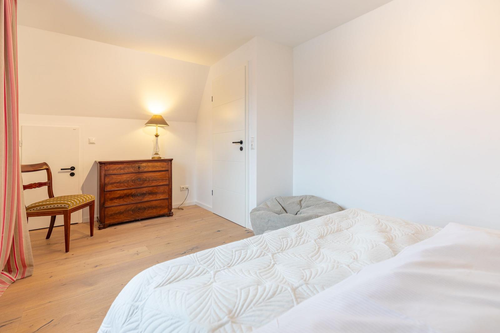 Schlafzimmer mit Bett, Schrank, Stuhl und Lampe.