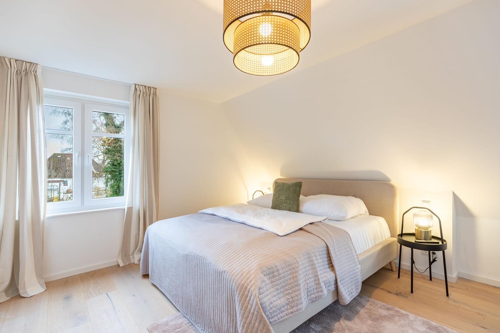 Schlafzimmer mit Bett, Fenster und Deckenleuchte.