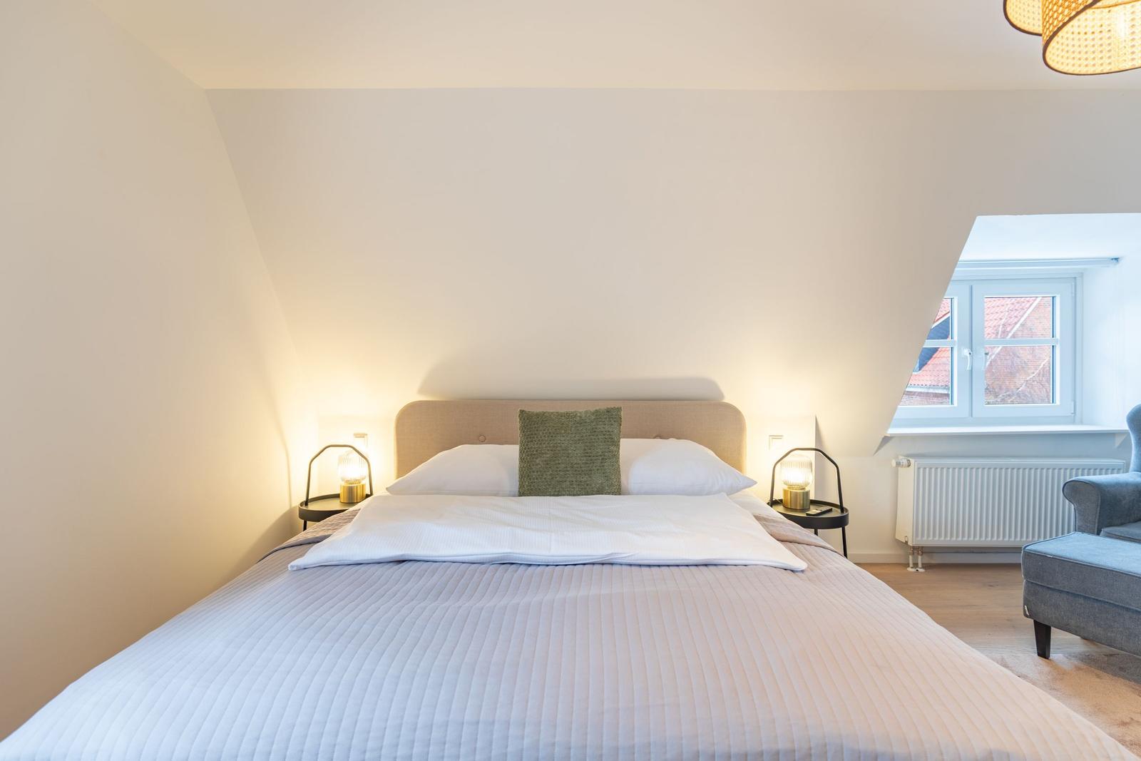 Doppelbett mit grünem Kissen, zwei Nachttische und Fenster.