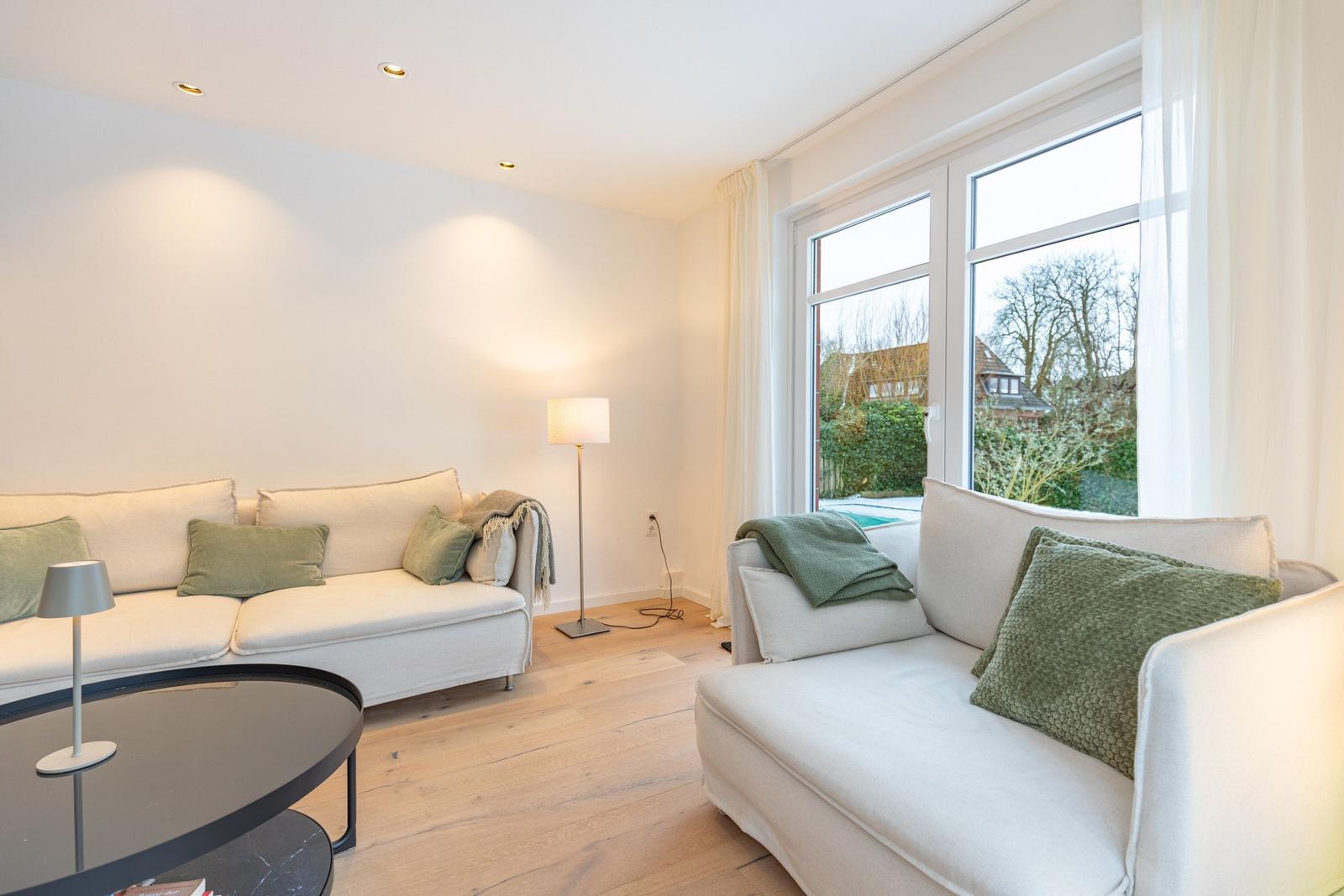 Wohnzimmer mit zwei Sofas, Tisch und Fenster mit Blick auf Garten.