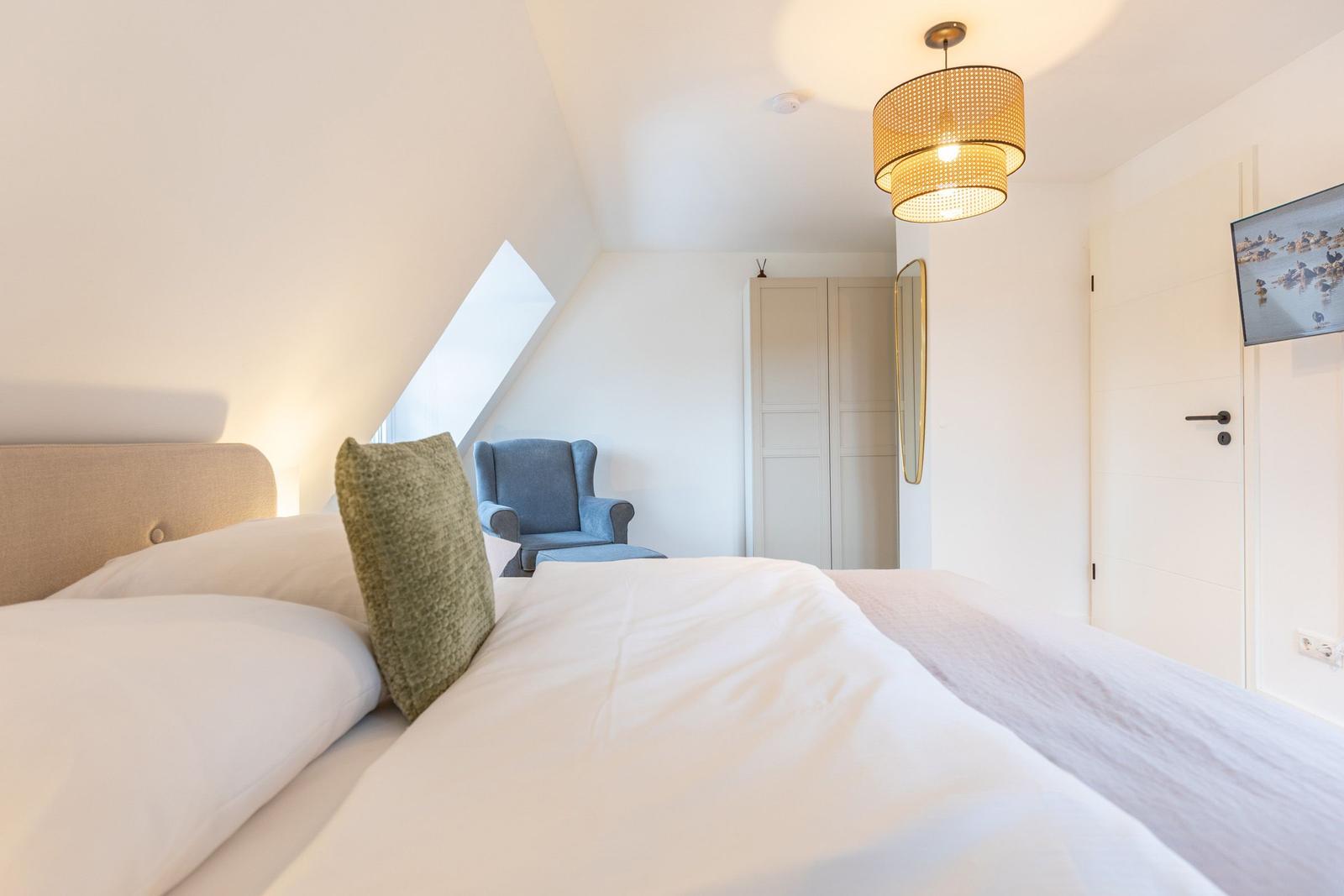 Schlafzimmer mit Dachschrägen, Bett, Sessel und Deckenlampe.