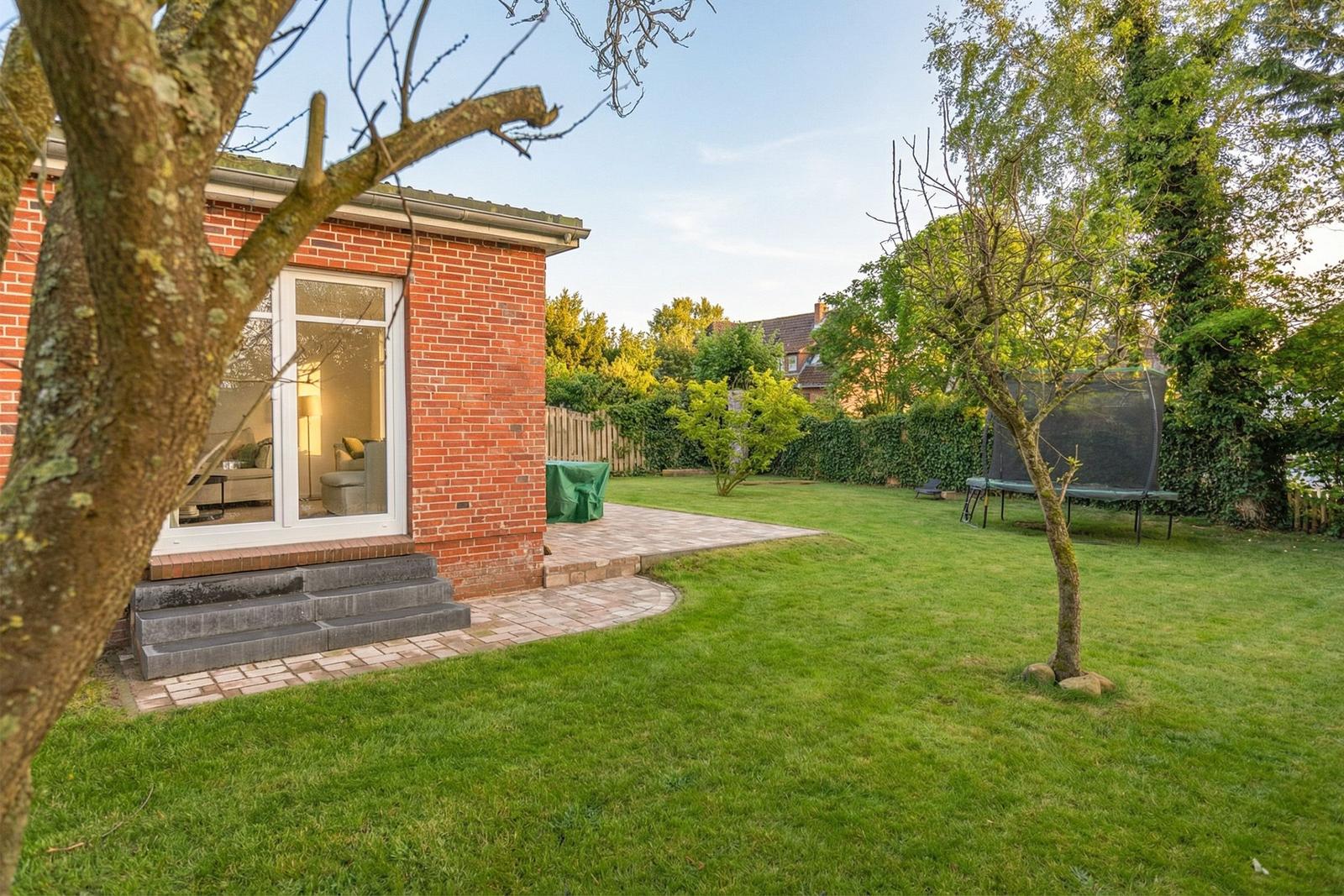 Rotes Backsteinhaus mit Terrasse und grünem Garten mit Trampolin.