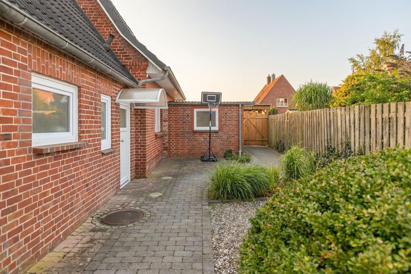 Hinterhof mit Basketballkorb, Steinweg und Hecken.
