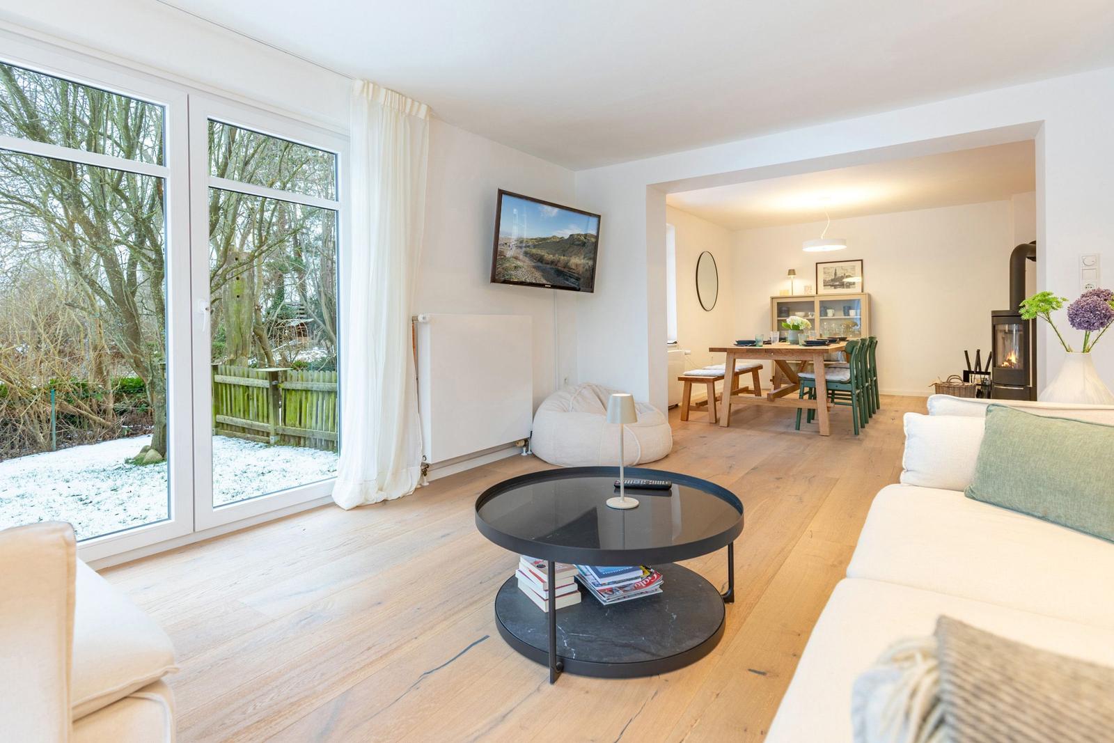 Wohnzimmer mit Sofa, Couchtisch und Fernseher. Durchgang zur Küche mit Esstisch und Kamin.