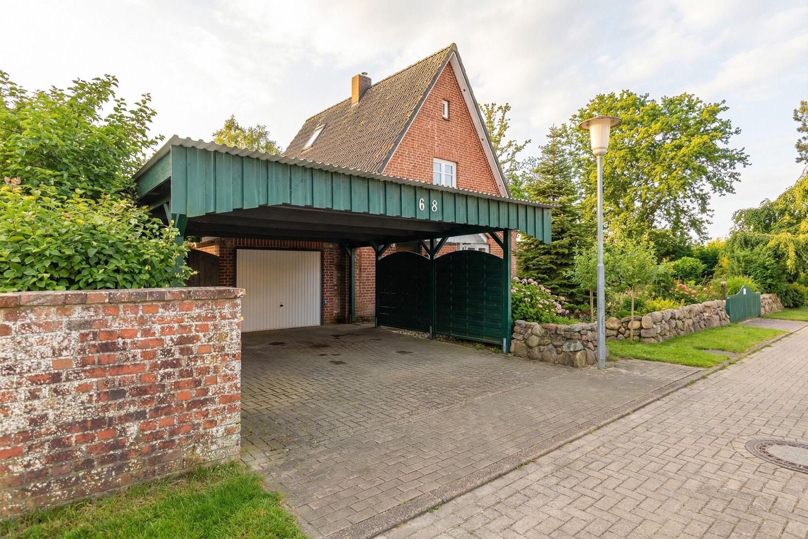 Haus mit Carport, Garagen- und Torbereich, umgeben von Grün und Steinmauern.
