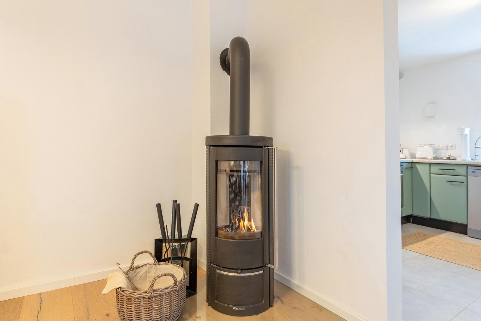 Kaminofen mit brennendem Feuer in einem Raum mit Holzboden und Blick in die Küche.